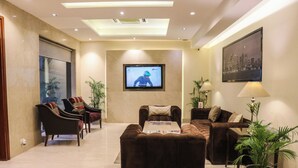 A modern living room with a flat-screen TV mounted on the wall, a brown leather sofa, a matching ottoman, and two armchairs. - Eternity (New Delhi)