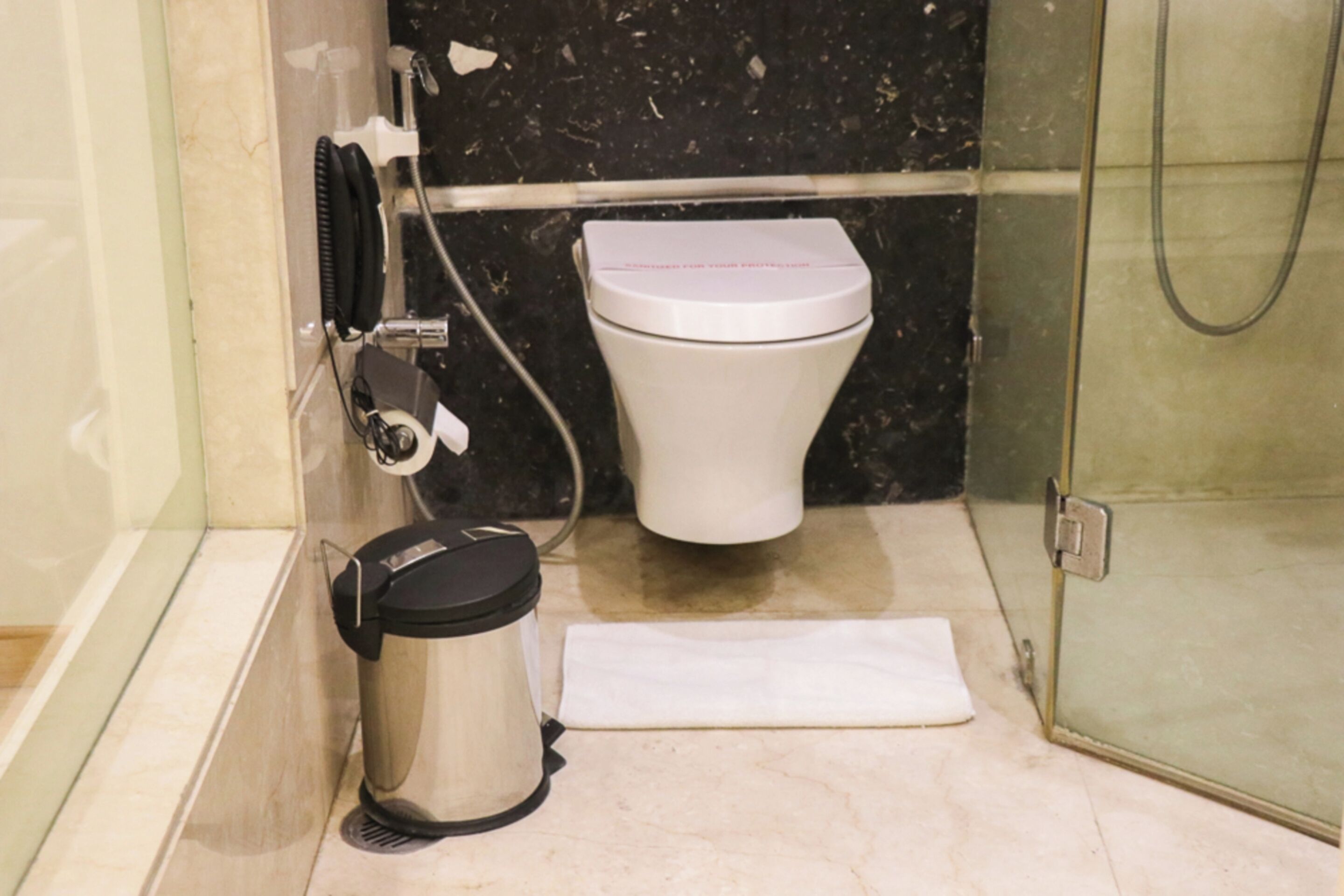 A bathroom with a toilet, a trash can, and a shower area.