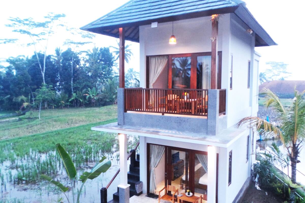A two-story building with a balcony, a dining area, and a view of a lush landscape.