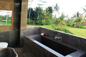 A modern bathroom with a large bathtub, a toilet, and a mirror. - Villa Kemuning Ubud (Tegallalang)