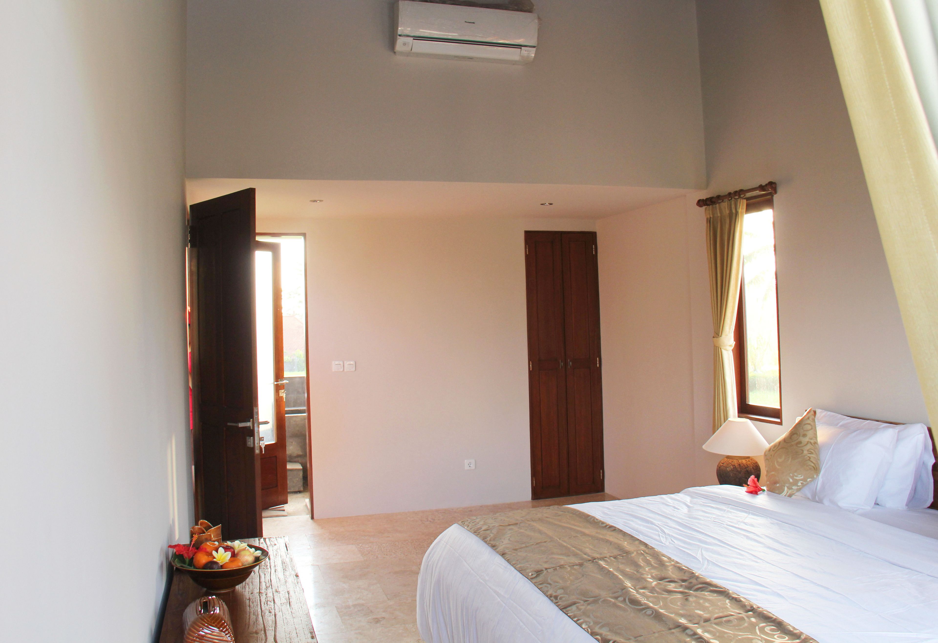 A hotel room with a bed, a bedside table with a lamp, a bowl of fruit, and a wardrobe.