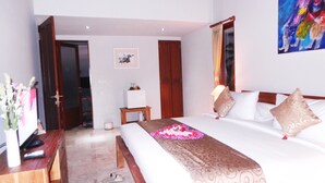 A hotel room with a bed, bedside tables, a desk, a chair, a door, and a painting on the wall. - Villa Kemuning Ubud (Tegallalang)