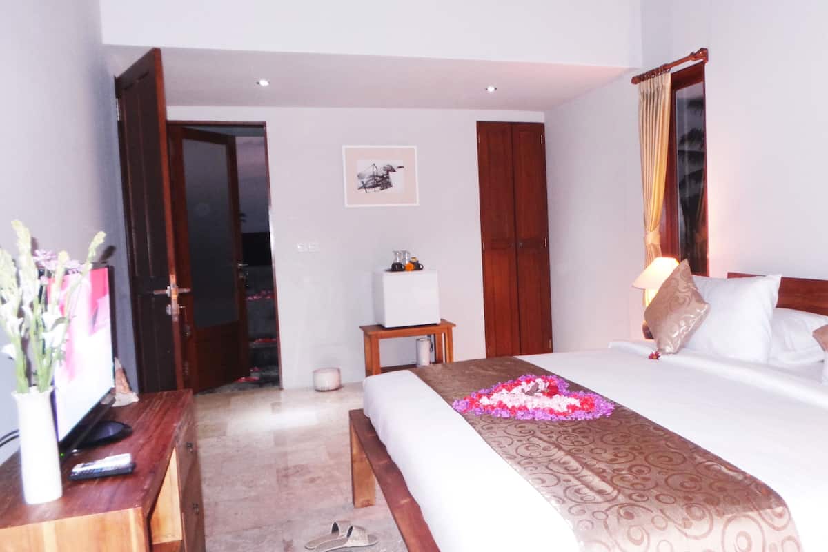 A hotel room with a bed, bedside tables, a desk, a chair, a door, and a painting on the wall.