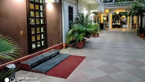 L’entrée d’un hôtel, avec une porte en bois sombre, des plantes en pot et un tapis rouge menant à l’entrée.