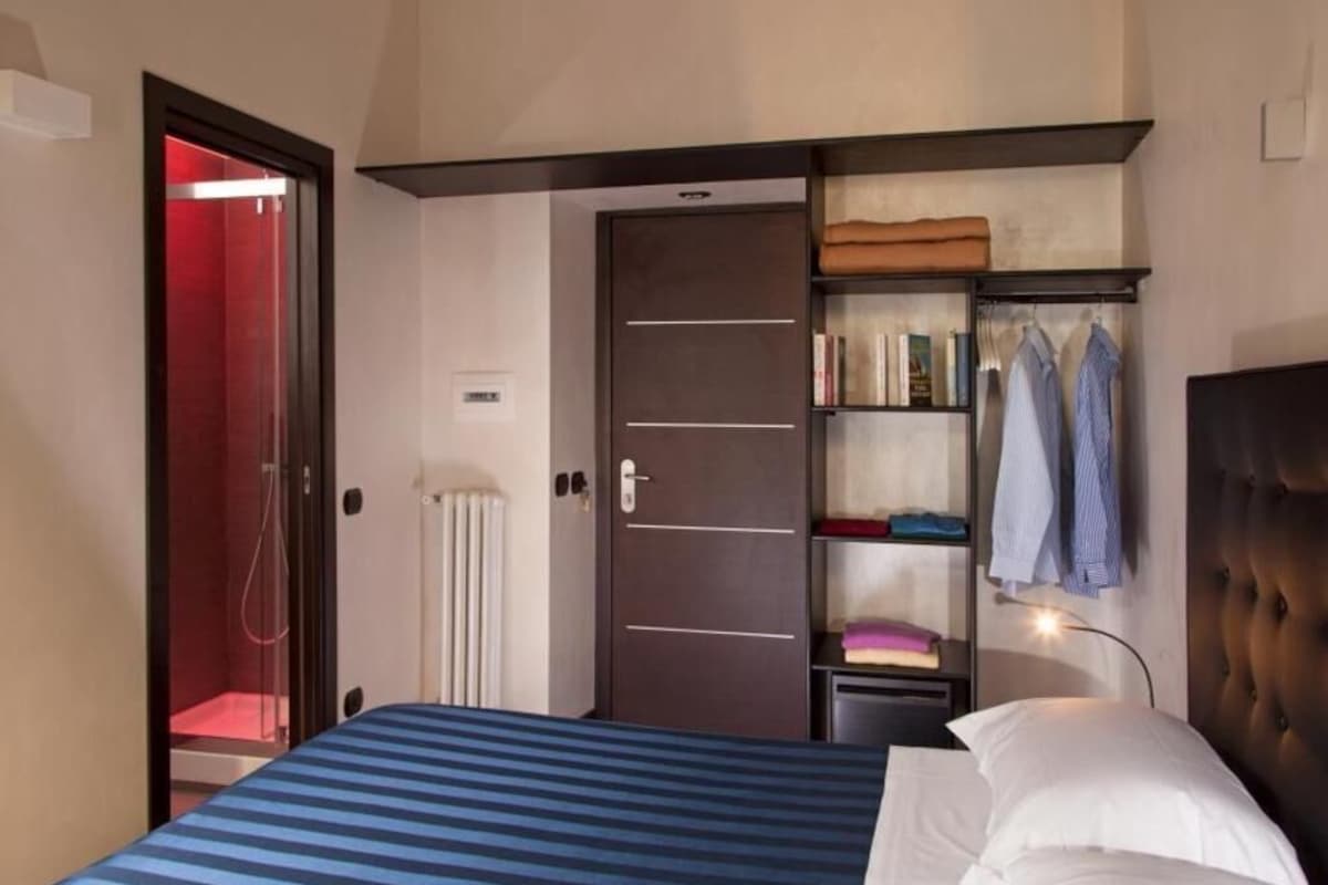 Une chambre à coucher comprenant un lit, une armoire, un radiateur et une porte donnant accès à une douche.