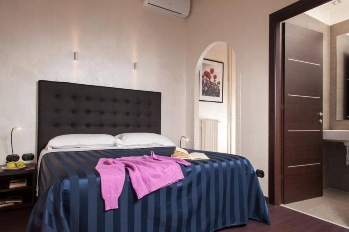 A bedroom with a large bed, a nightstand, a bedside table, and a door leading to a bathroom.