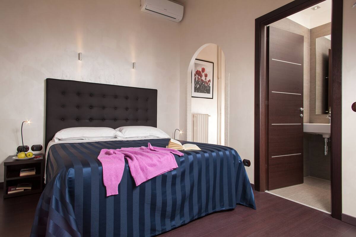 A neatly made bed with a striped bedspread, a bedside table with a lamp, and a framed picture on the wall.