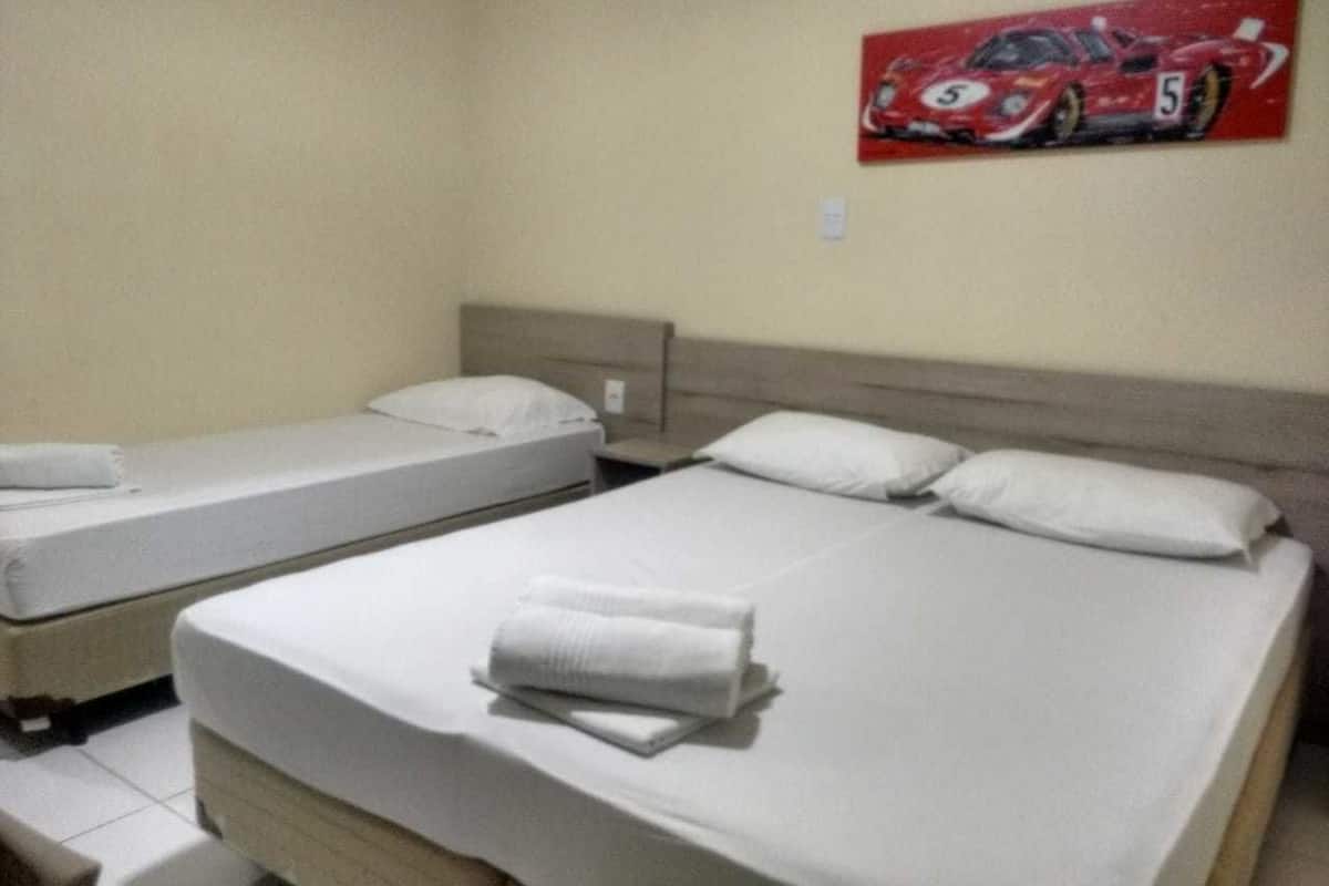 A hotel room with two single beds and a larger double bed, each with white linens and pillows.