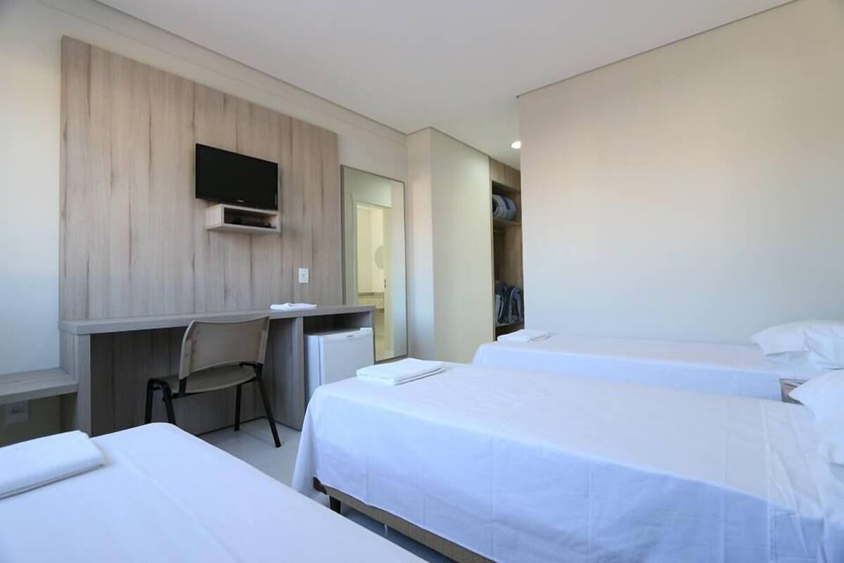 A hotel room with two beds, a desk, a chair, a TV, and a wardrobe.