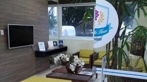 Un vestíbulo moderno con televisión de pantalla plana, un mostrador de recepción, asientos amarillos y una planta grande en maceta.