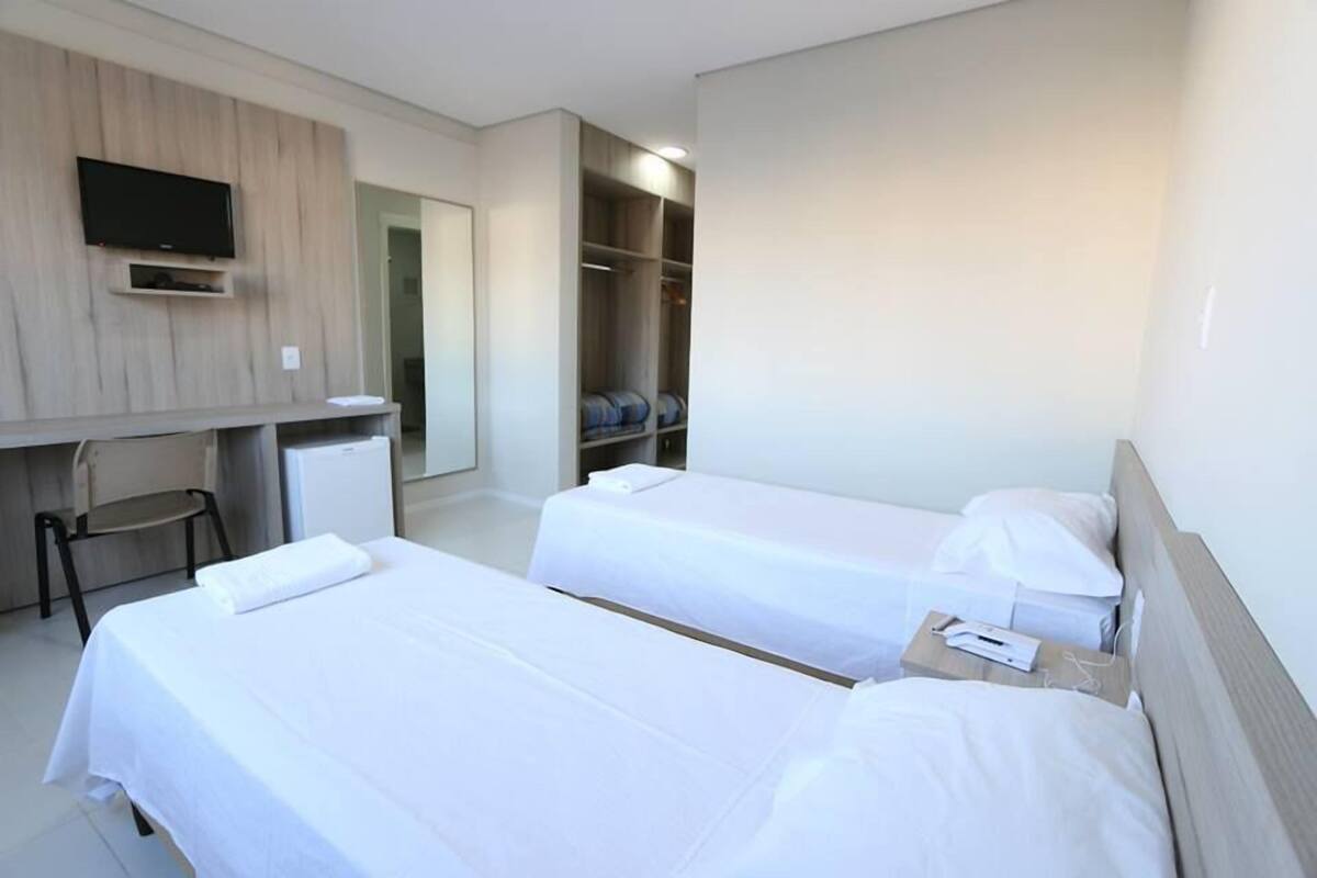 A hotel room with two beds, a desk, a TV, and a wardrobe.
