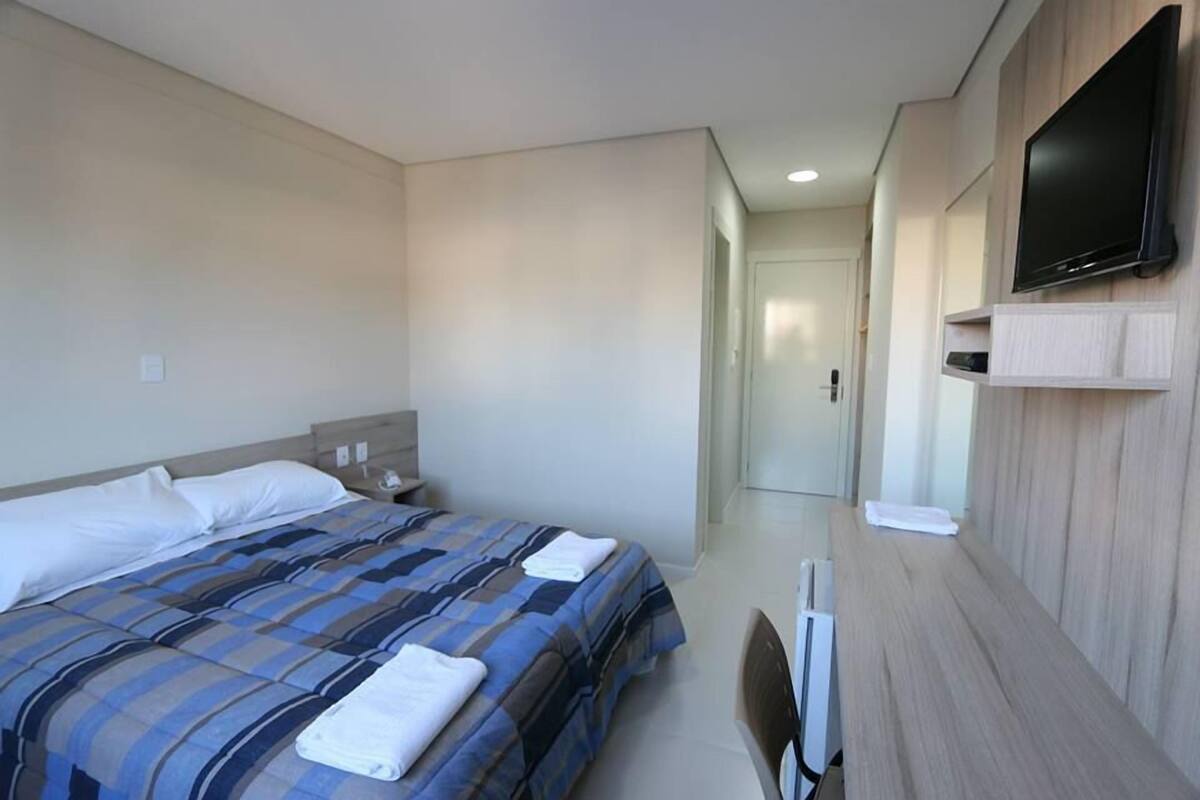 A hotel room with a bed, a TV mounted on the wall, and a desk with a chair.