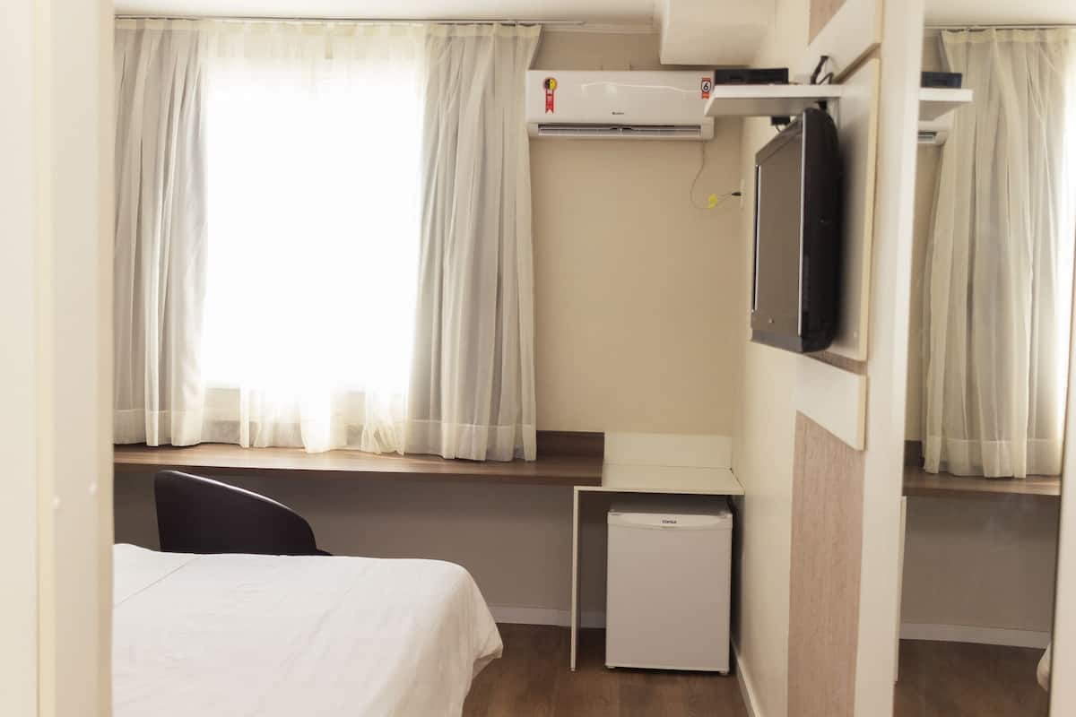 Ein Hotelzimmer mit einem Bett, einem kleinen Schreibtisch, einem Fernseher und einer Klimaanlage.