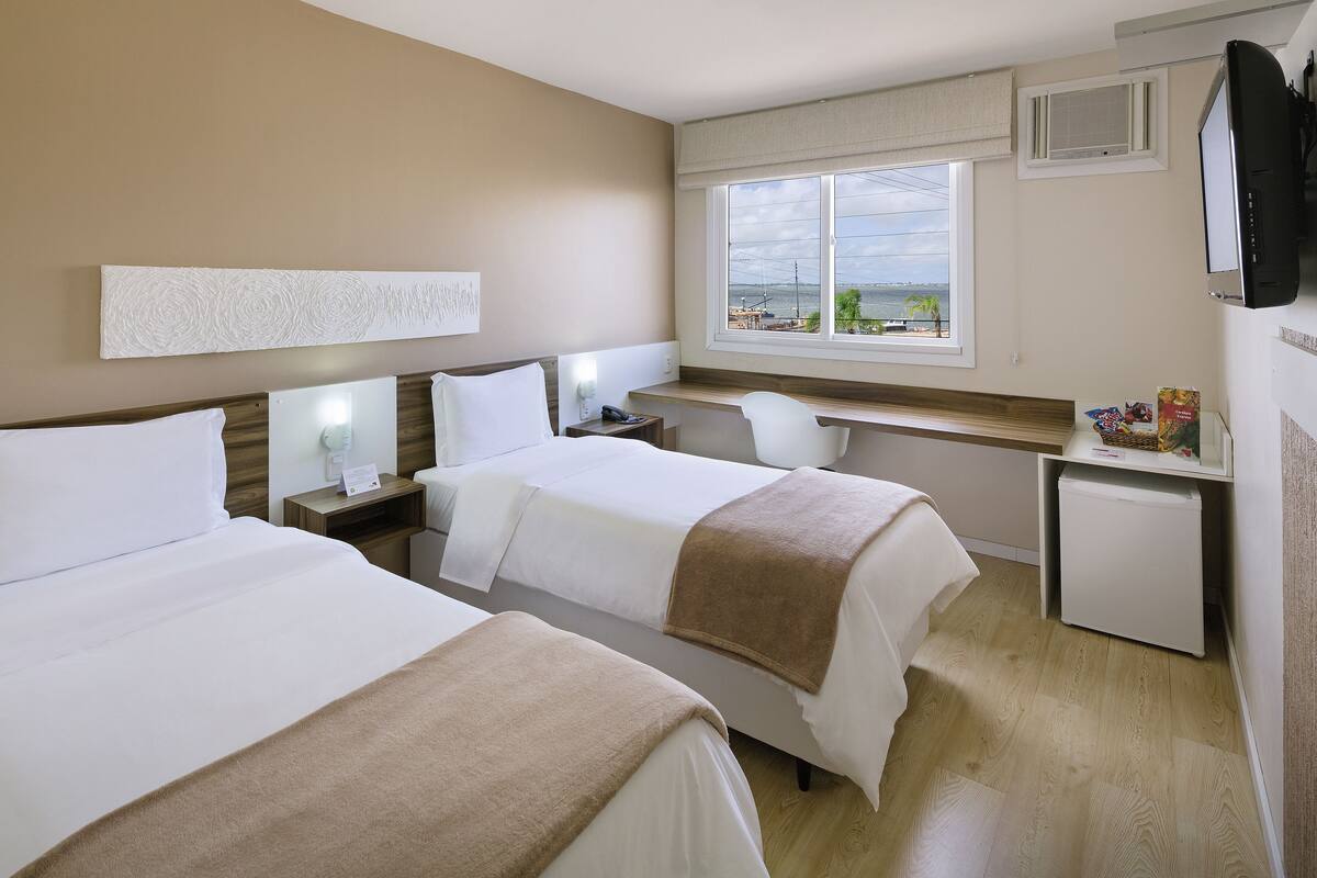Ein Hotelzimmer mit zwei Betten, einem Schreibtisch, einem Sessel, einem Fernseher und einem Fenster mit Blick.