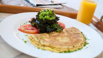 Un plato con tortilla, tomate y lechuga, además de un vaso de zumo de naranja sobre una mesa.