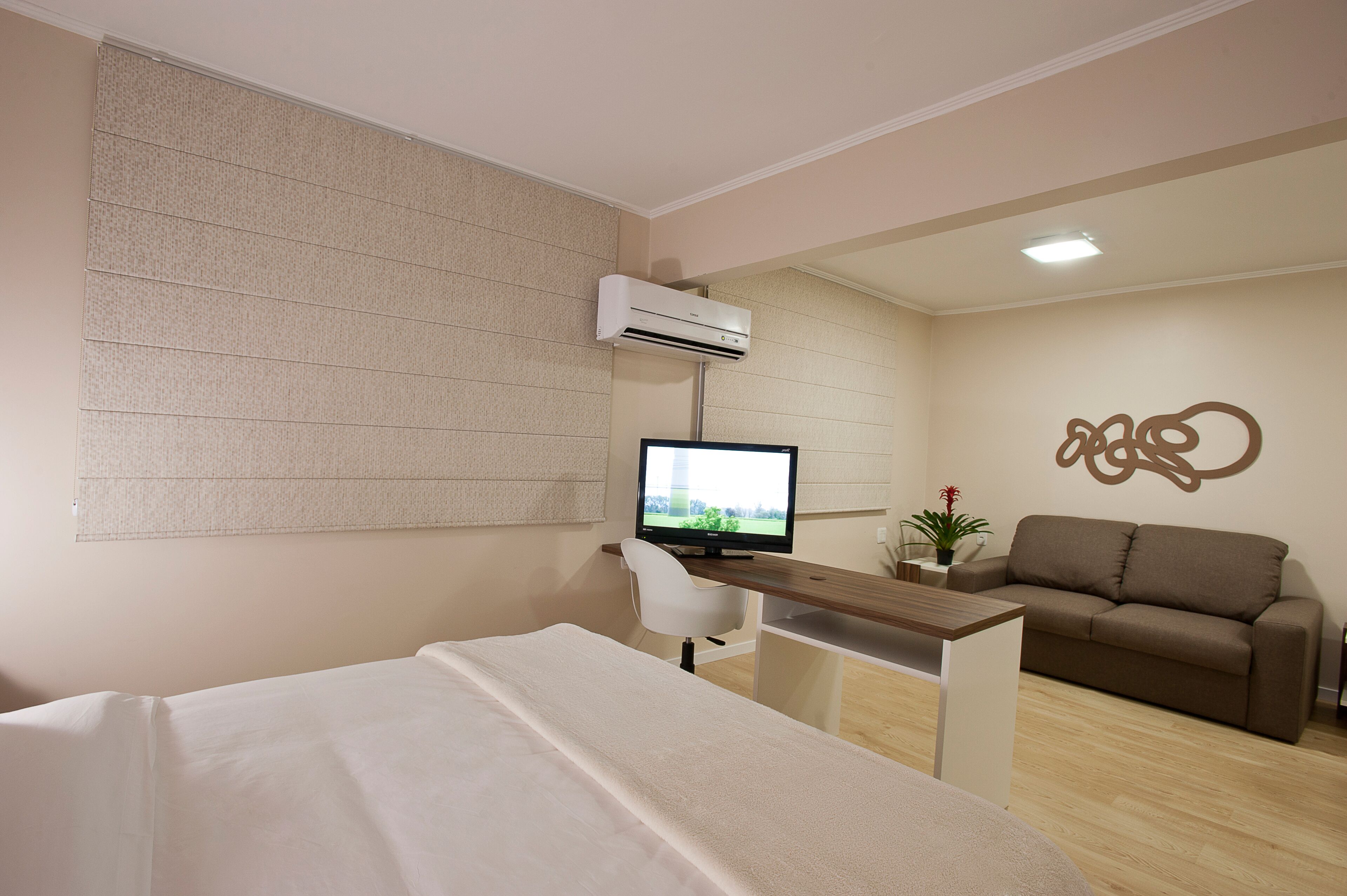 A modern hotel room with a bed, a desk with a computer, a sofa, and an air conditioning unit.