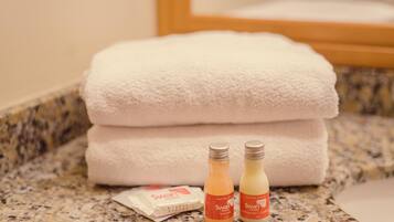 A bathroom with a granite countertop, two bottles of Swan hotel shampoo, and a white towel.
