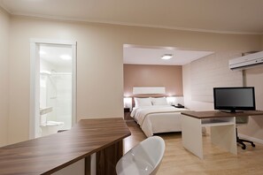Une chambre d’hôtel avec un bureau en bois, une chaise blanche, un lit, une douche et un téléviseur.