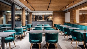 Ein modernes Restaurant mit Petrolfarbenen Stühlen und Tischen, Holzboden und einer großen Bildschirmwand.