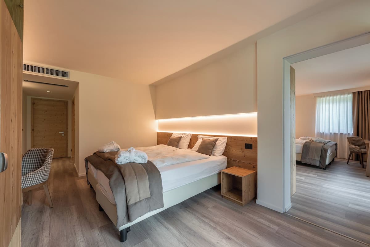 A modern hotel room with a large bed, bedside tables, a chair, and a wooden floor.