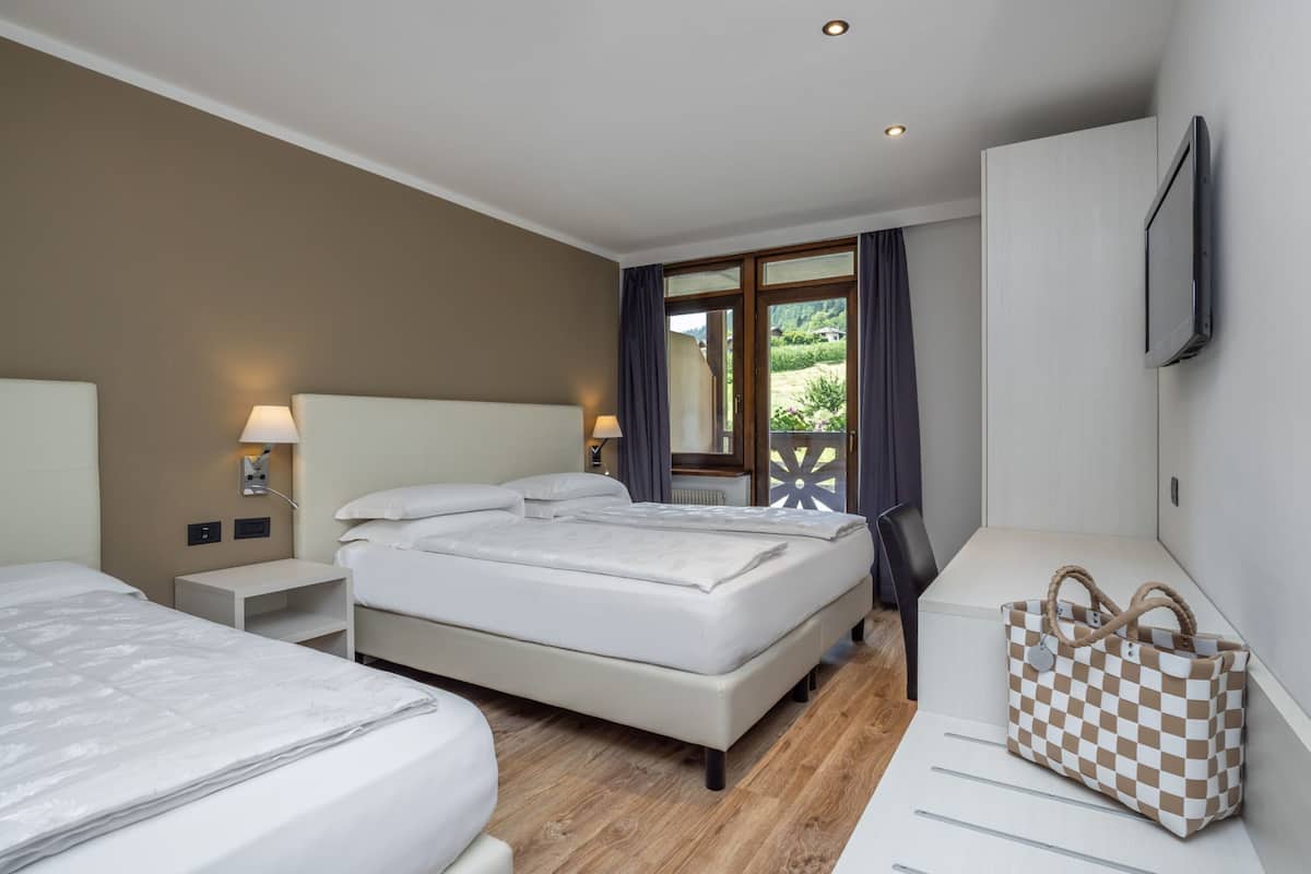 A hotel room with a large bed, a desk, a chair, a TV, and a view of the outdoors.