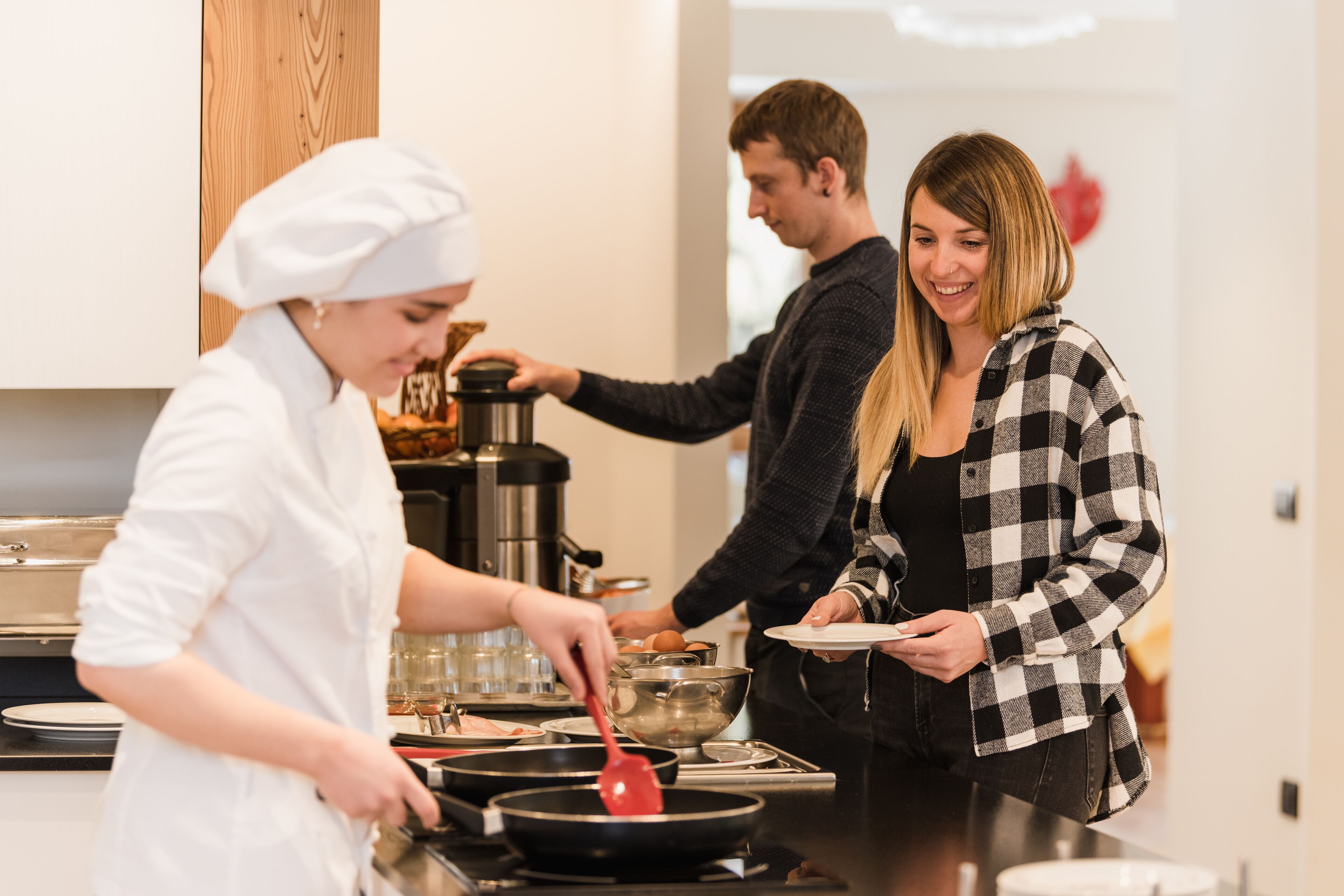 A modern kitchen with a chef preparing food, a coffee machine, and a dining area with a table and chairs.