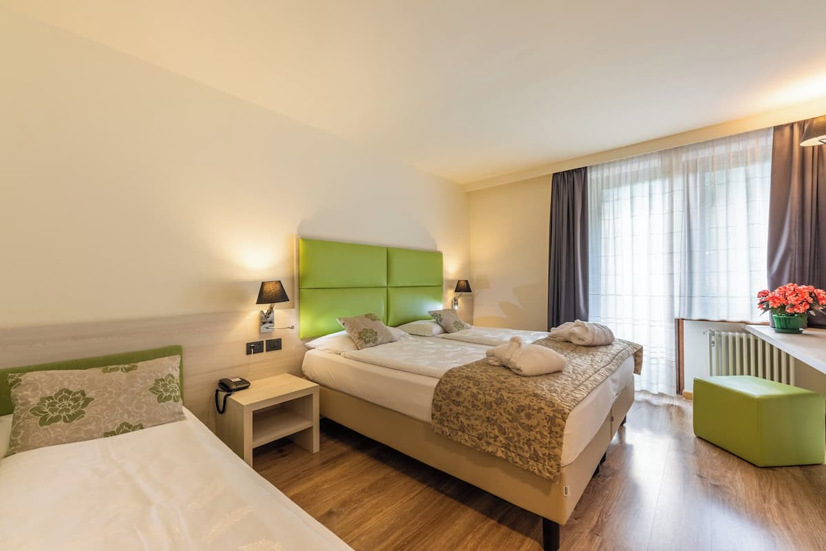 A hotel room with a bed, bedside tables, lamps, a radiator, and a window with curtains.