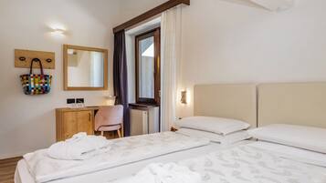 A hotel room with a bed, a wooden dresser, a mirror, a hanging bag, and a window with curtains.