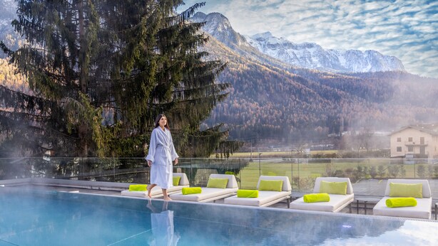 Eine Person geht an einem Pool mit Liegestühlen entlang, mit Blick auf die Berge.
