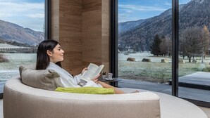 Eine Person liest ein Buch in einem modernen Zimmer mit großen Fenstern und Blick auf eine gebirgige Landschaft.