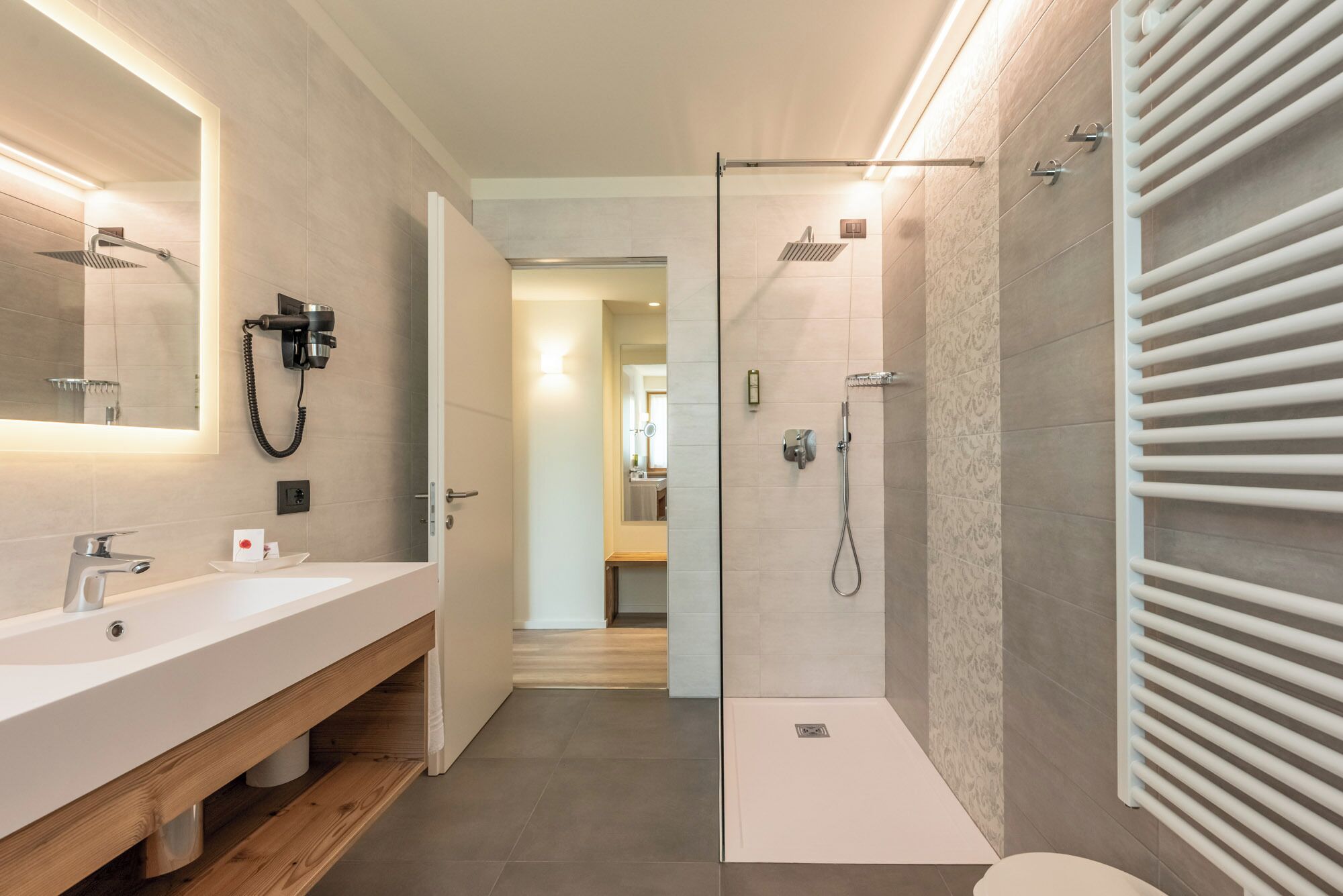 A modern bathroom with a large mirror, dual sinks, a shower, and a towel rack.