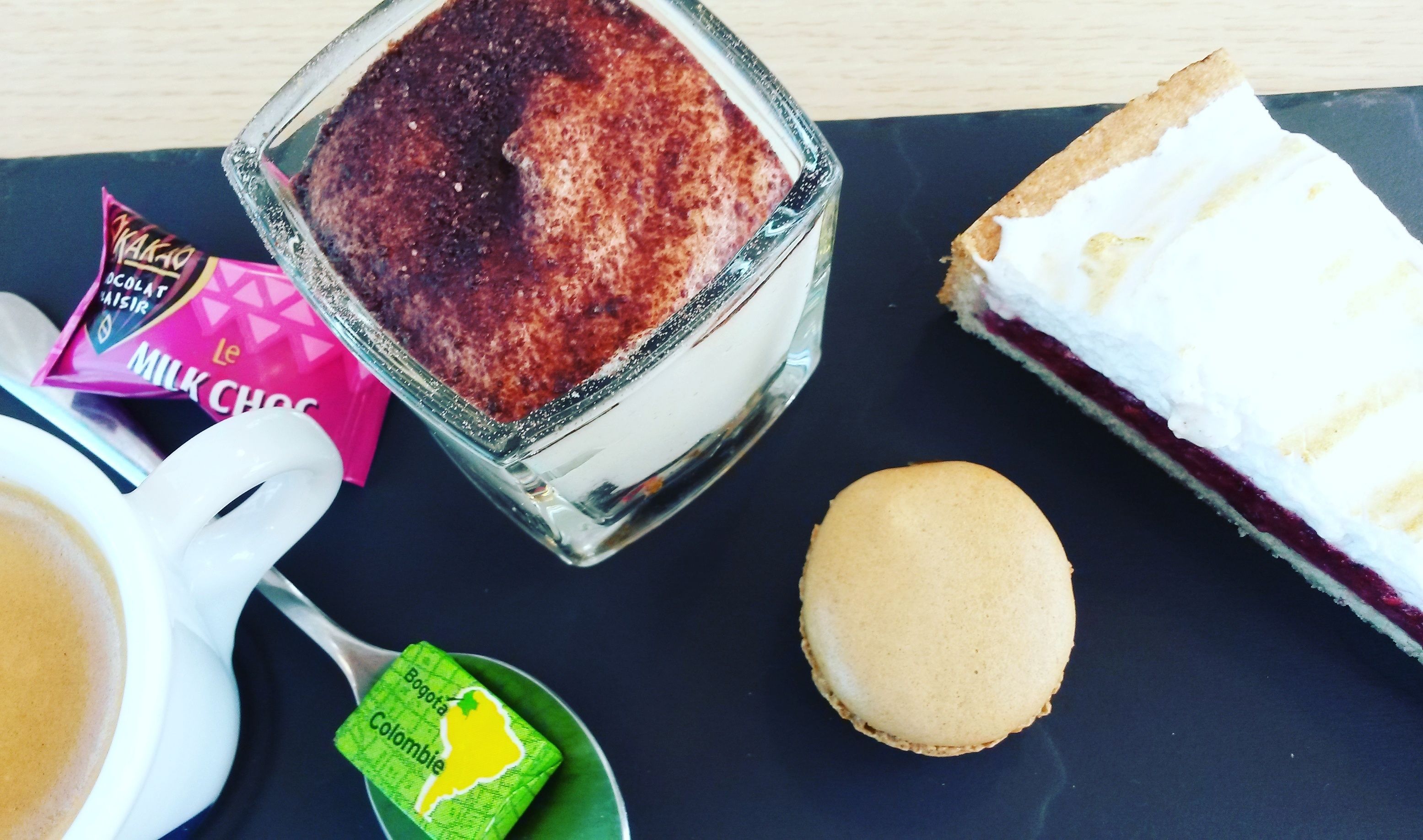 A dessert tray with a chocolate mousse, a slice of cake with white frosting, a biscuit, a packet of milk chocolate, and a cup of coffee.