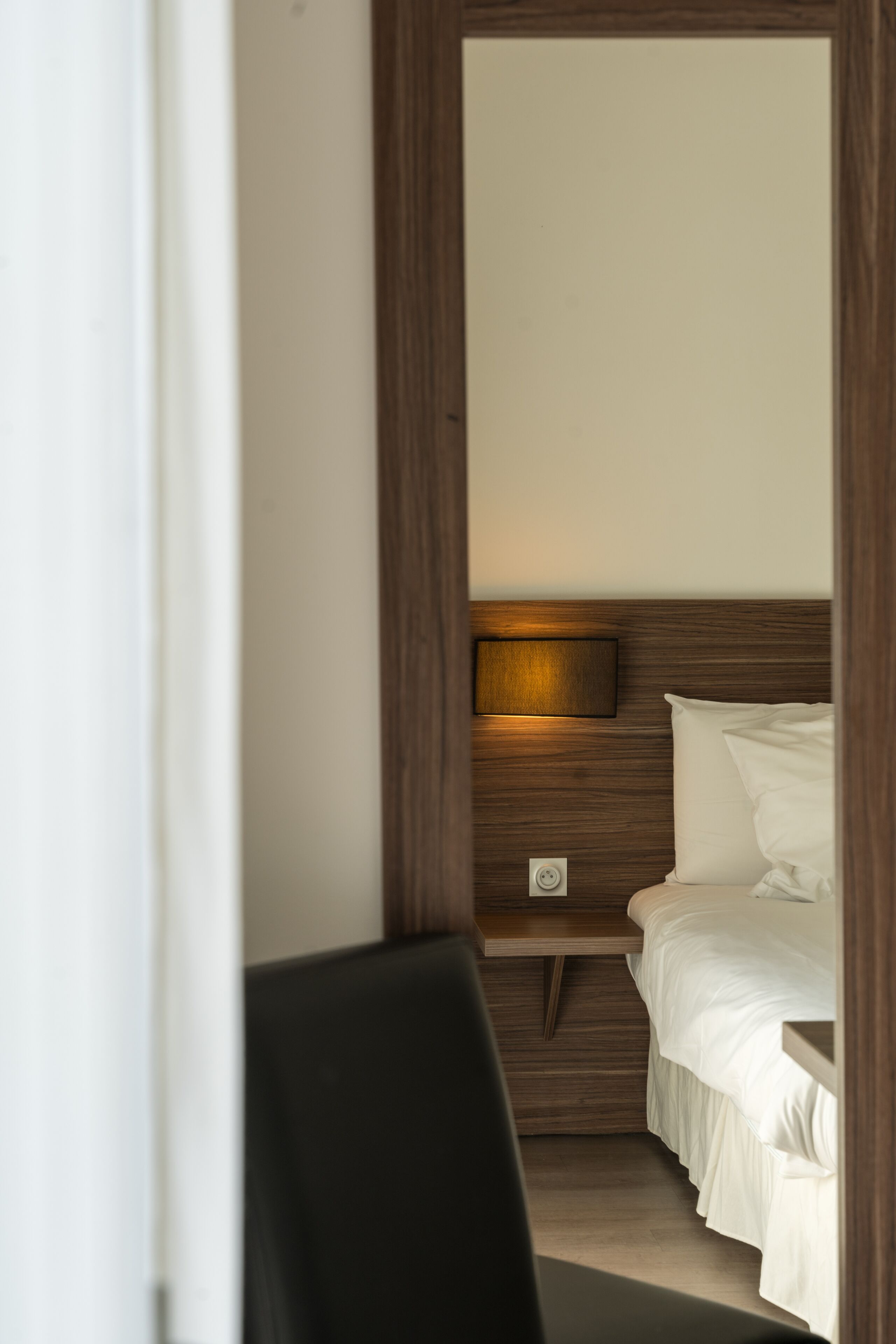 A hotel room with a wooden headboard, a bedside table, a lamp, and a bed.
