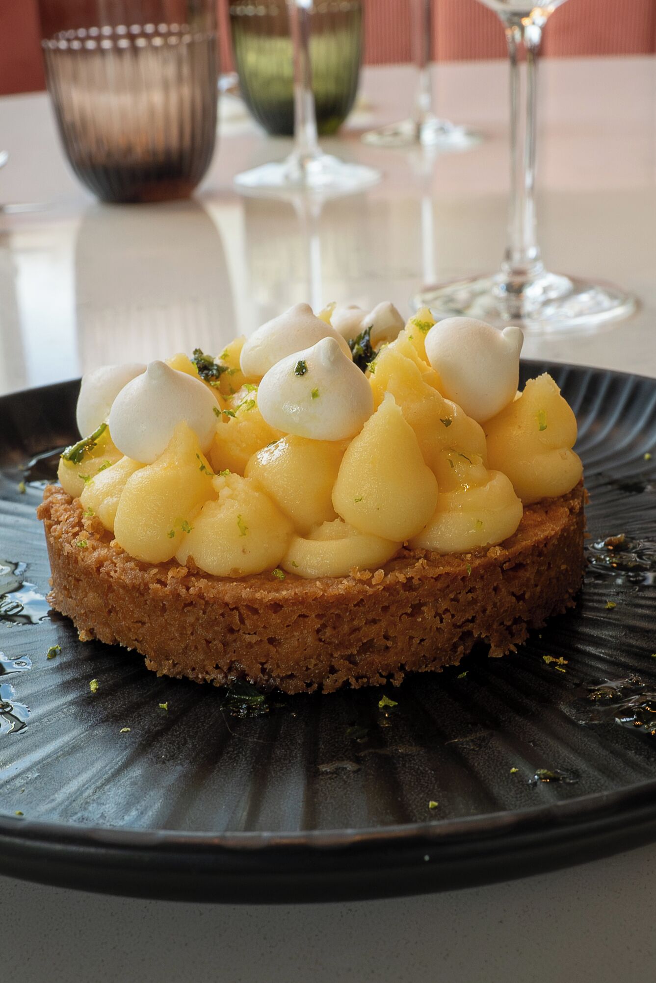 Un postre en un plato con borde texturizado, sobre una mesa con un vaso y una vela al fondo.