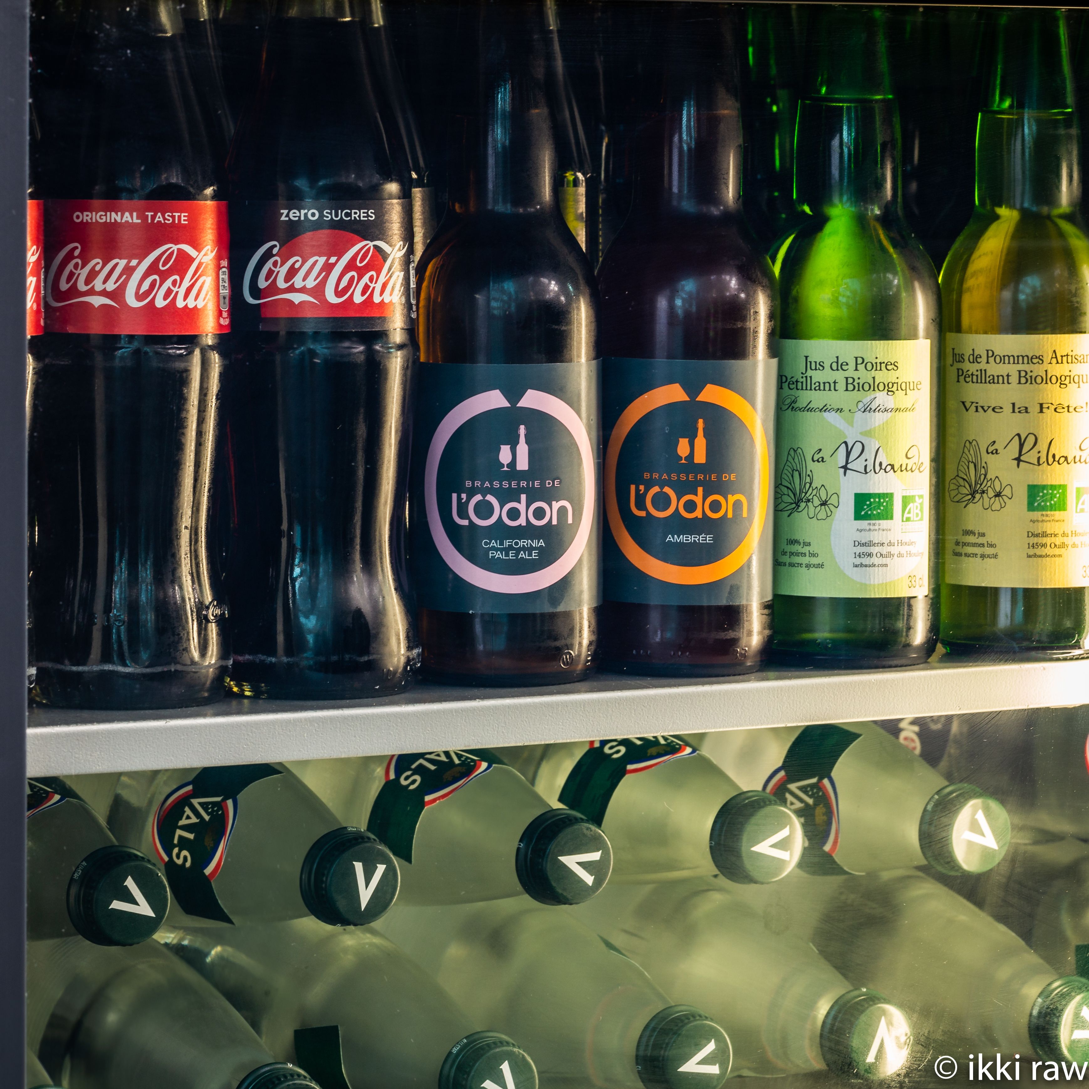 A refrigerated display of beverages including Coca-Cola, L'Odon Pale Ale, and Jus de Poires.