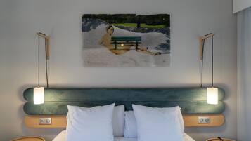 A hotel room with a bed, white pillows, a headboard, bedside tables, a remote control, and a painting of a park scene.