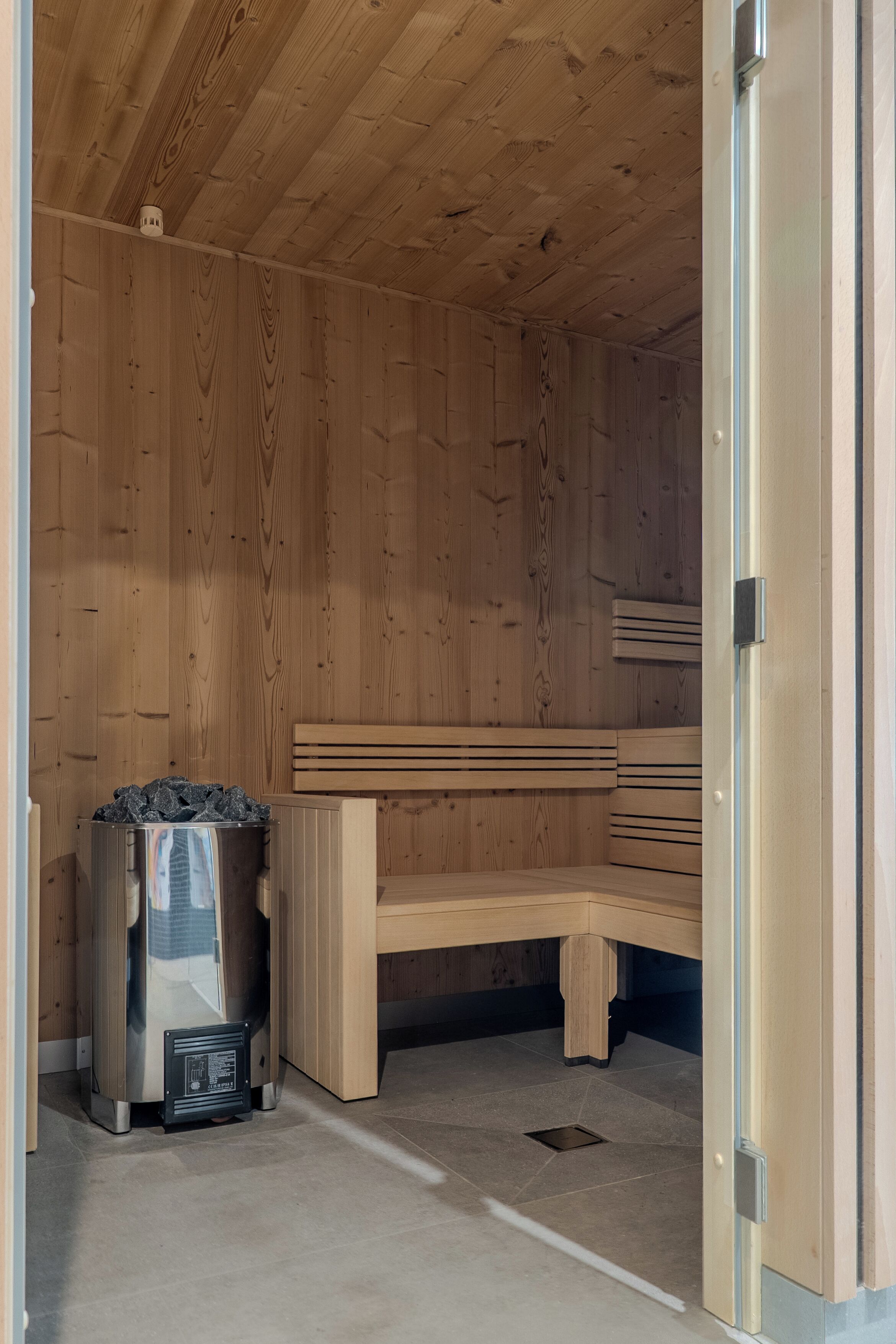 A sauna room with wooden walls, benches, and a sauna unit.