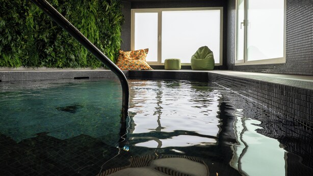 Una piscina interior con agua cristalina, una pared verde y una ventana con luz natural.