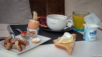 A breakfast setting with croissants, a plate of sausages, a glass of orange juice, a cup of coffee, and a container of yogurt.