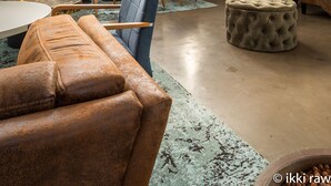 Un interior moderno con techos altos, una zona de estar central con un sofá y sillones, una mesa redonda y una planta grande en maceta.
