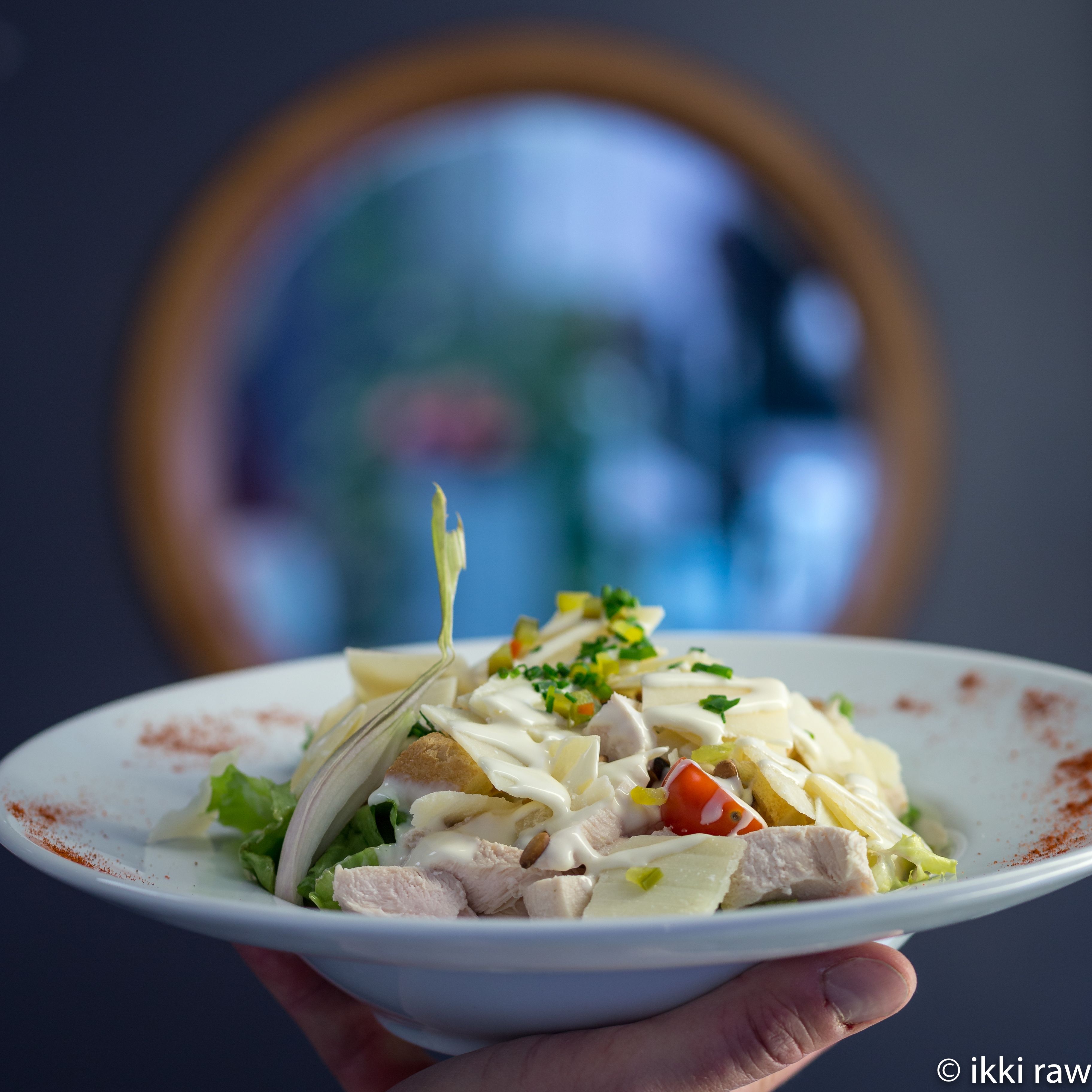 Une assiette de salade composée de divers ingrédients, accompagnée d’une sauce crémeuse, tenue par une personne.