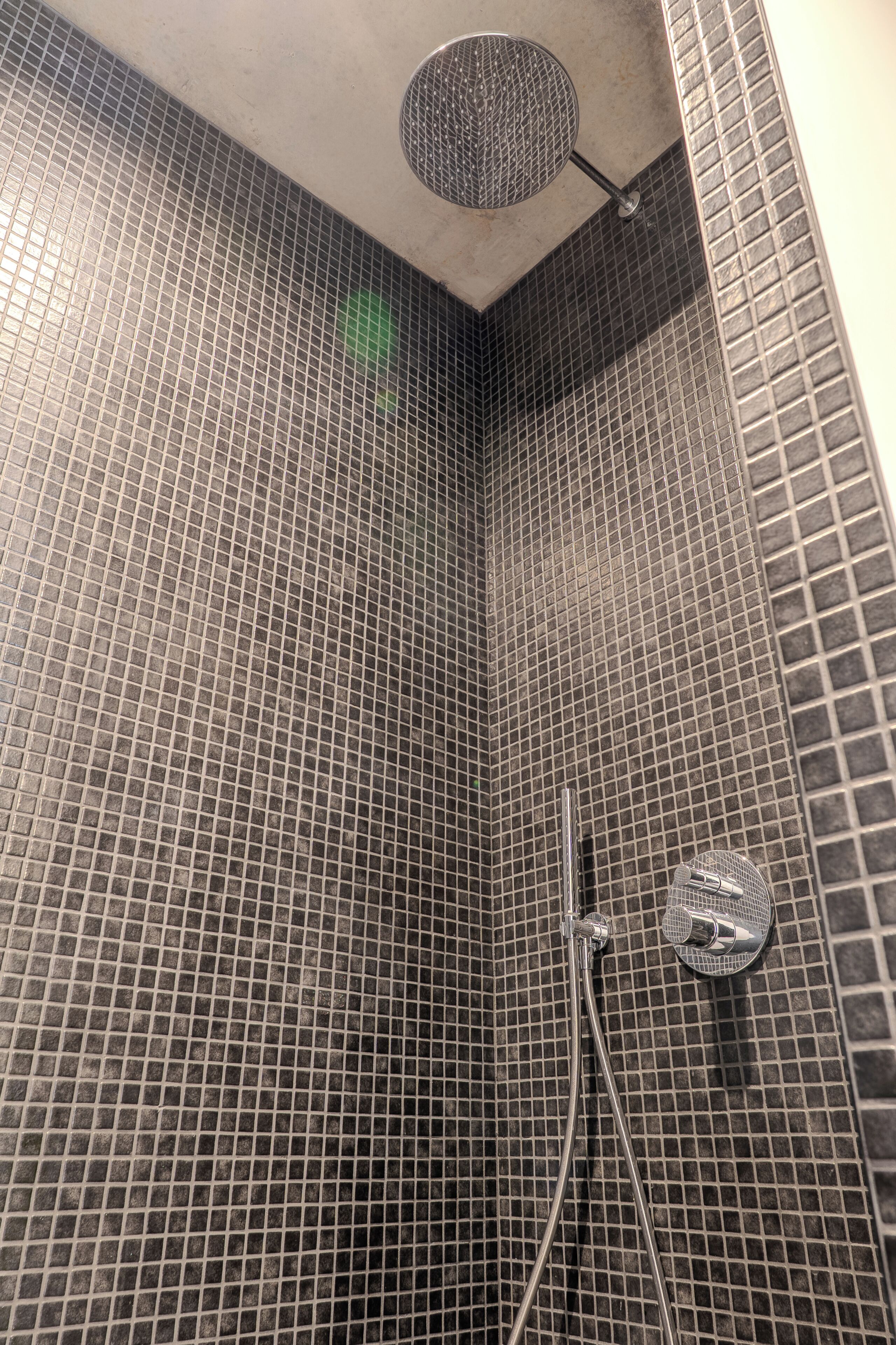 A shower area with a tiled wall and a handheld showerhead.