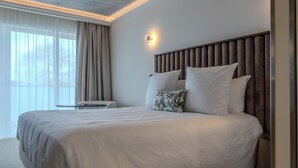 Habitación de hotel moderna con una cama grande, una mesita de noche, una lámpara de pared y vistas a árboles por la ventana.
