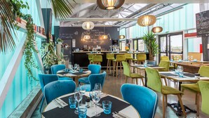 Un restaurante moderno con sillas azules y verdes, una zona de bar y un menú en la pizarra.