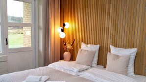 Habitación de hotel con una cama grande, un florero con flores secas y una lámpara de pared.