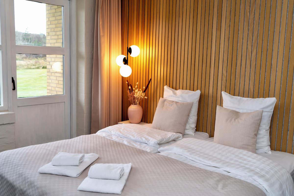 Habitación de hotel con una cama grande, un florero con flores secas y una lámpara de pared.