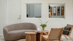 Una sala moderna con un sofá, una silla, una mesita y un florero con flores. Hay dos lámparas colgantes y una ventana con vistas.