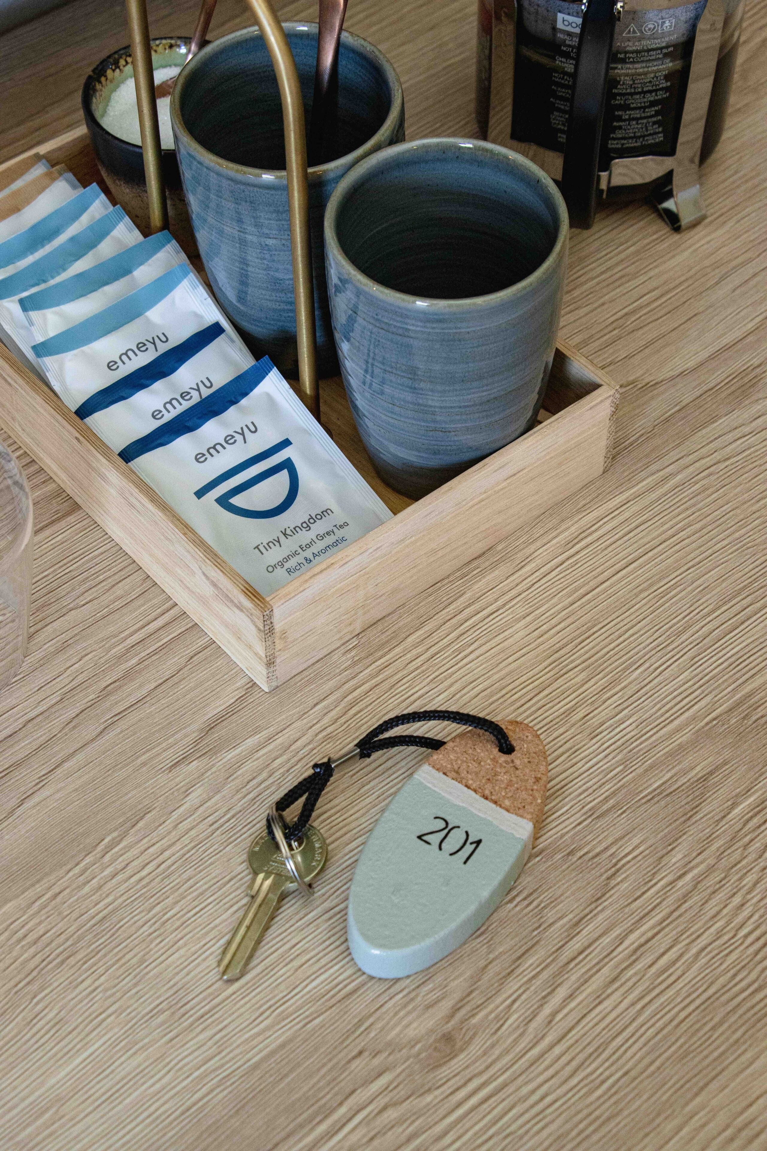 Una bandeja de madera con tres tazas de cerámica, una bolsita de té y un llavero con un adorno.