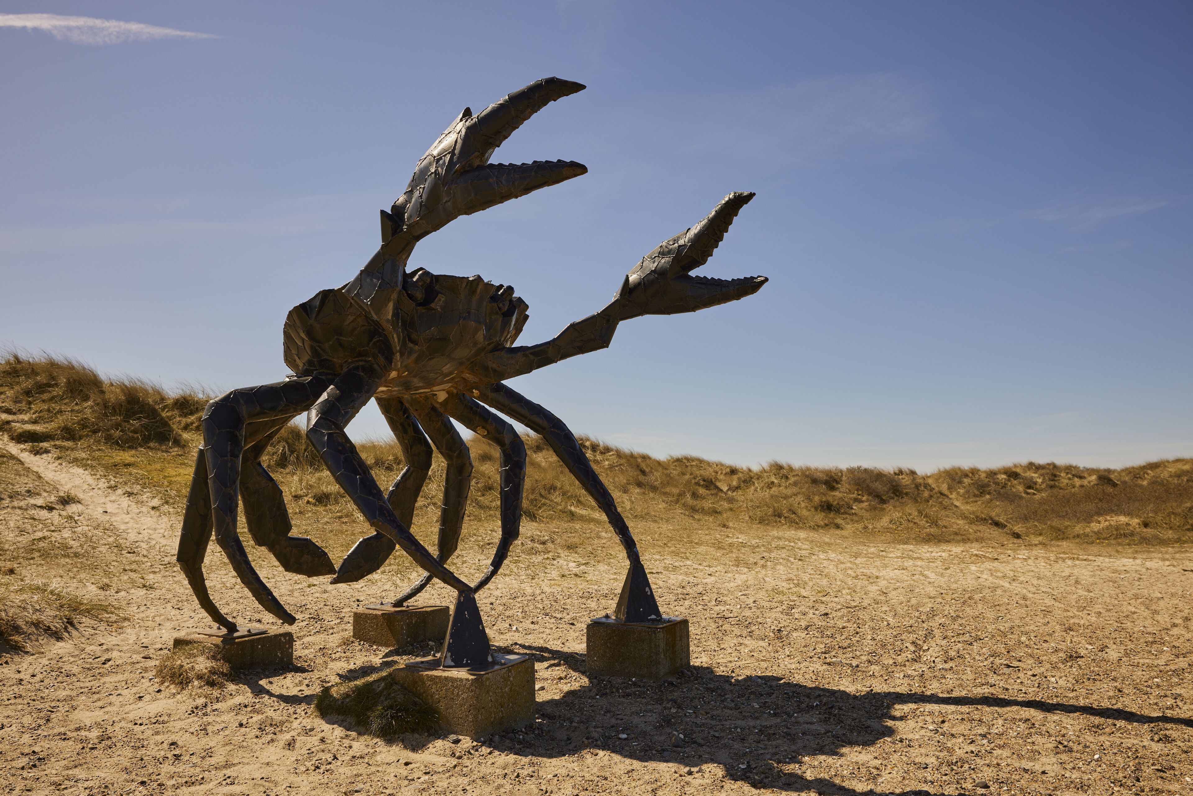 A metal sculpture of a crab on concrete blocks in a sandy area.