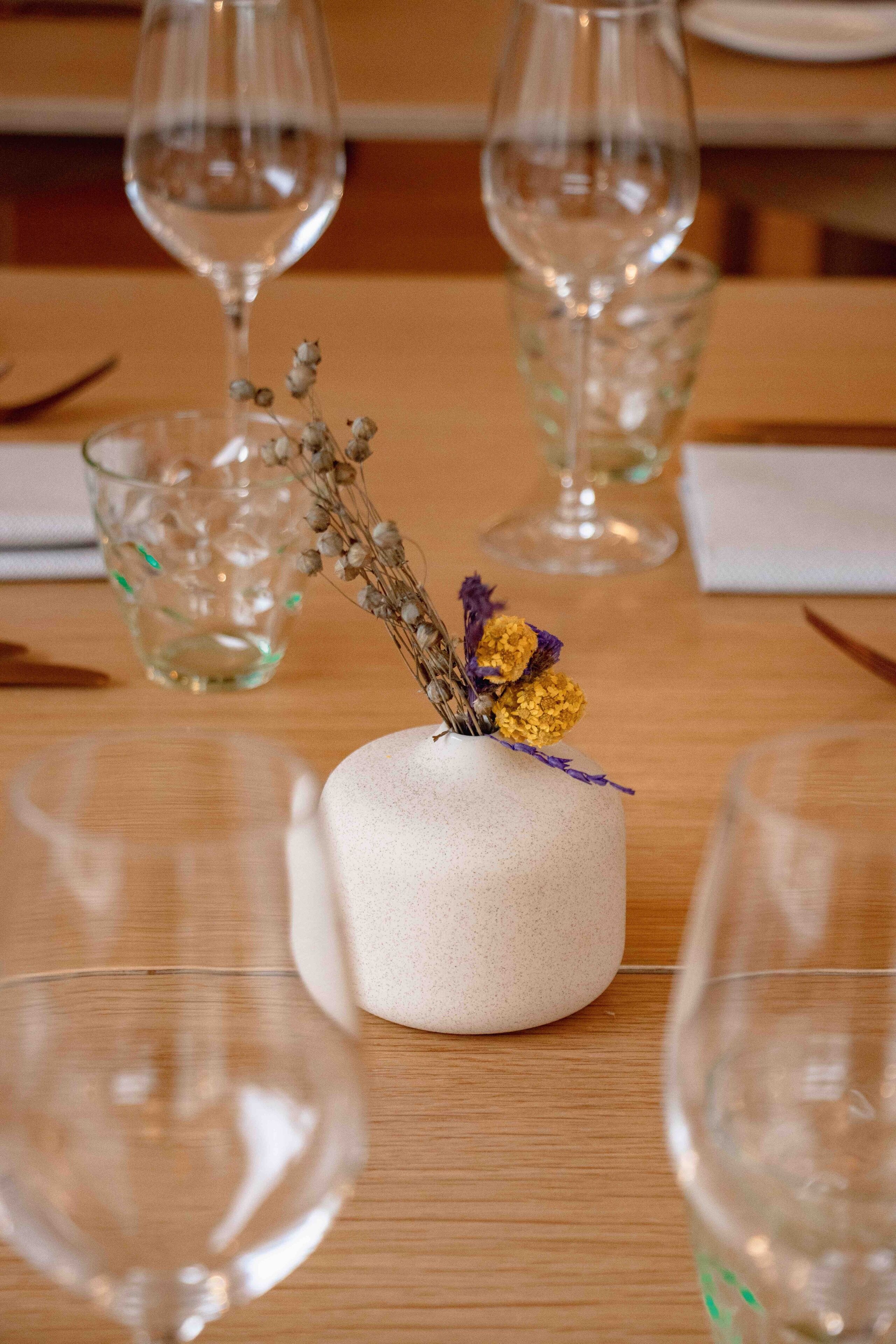 Una mesa con un pequeño florero texturizado que contiene flores secas y una ramita de verdor.